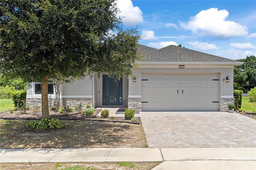 A single-story house with a stone-accented facade, a paved driveway, and a large front tree — 8113 BRIDGEPORT BAY CIRCLE, MOUNT DORA, FL