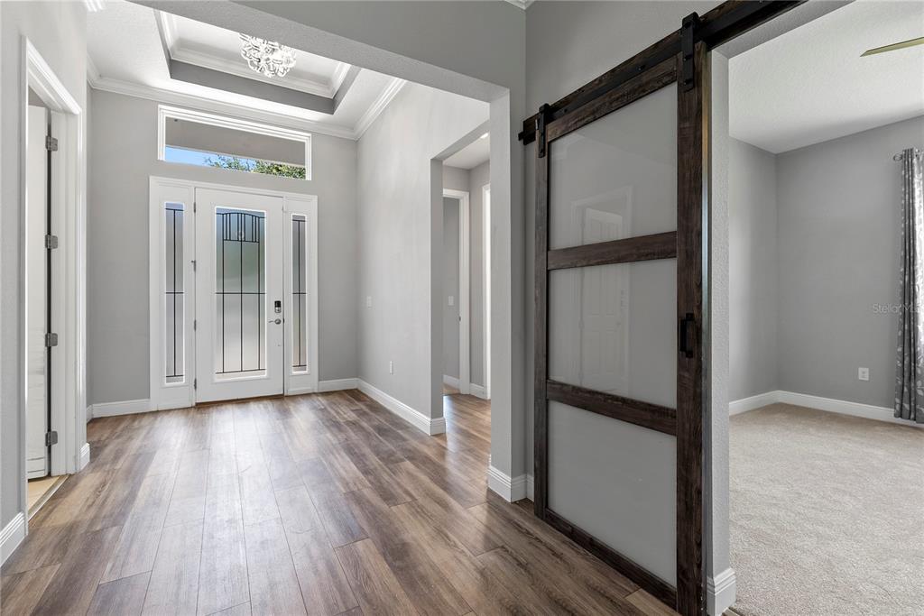 A hallway with gray walls and wood-look flooring leads to a room with sliding barn doors — 8113 BRIDGEPORT BAY CIRCLE, MOUNT DORA, FL
