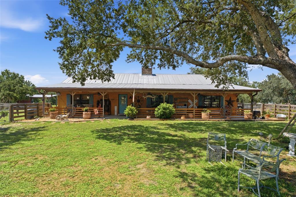 A single-story brick house with a metal roof and a wide front porch sits behind a lawn — 7674 SW ENVIRONMENTAL LAB STREET, ARCADIA, FL
