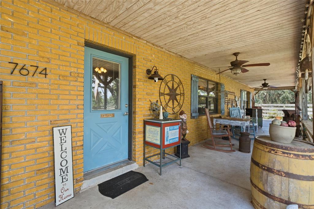 A covered brick porch features a blue front door, ceiling fans, and rustic decor — 7674 SW ENVIRONMENTAL LAB STREET, ARCADIA, FL