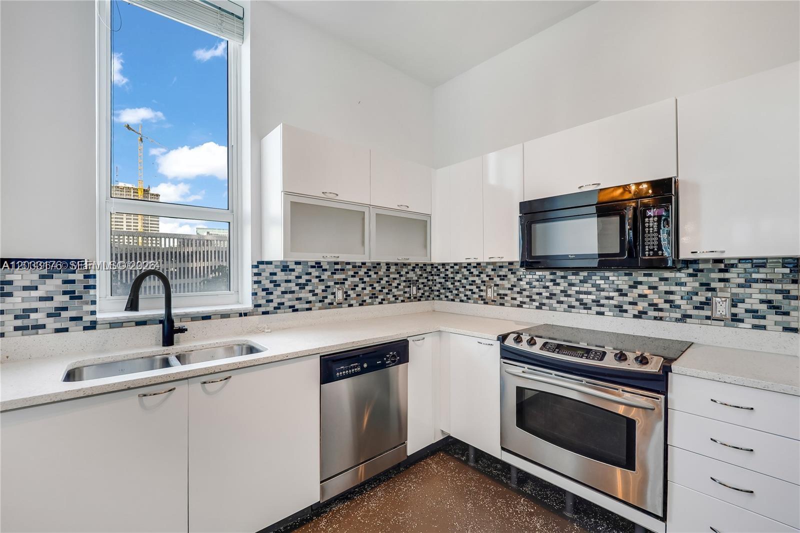 A kitchen features white cabinets, stainless steel appliances, a mosaic backsplash, and a large window — 234 NE 3rd St # 507, Miami FL 33132, MIAMI, FL