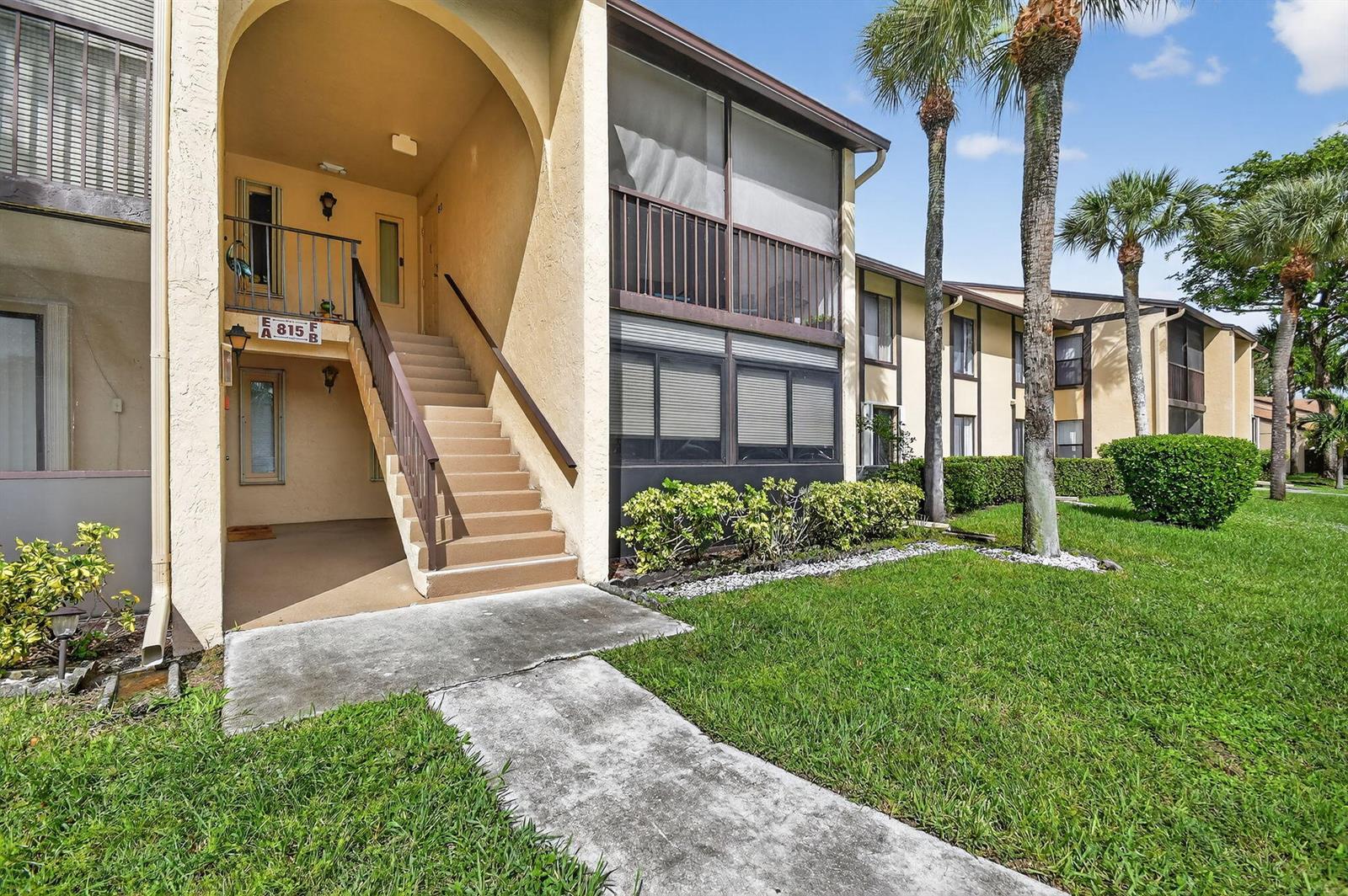 An exterior view of a two-story apartment building with a concrete staircase and palm trees — 815 Sky Pine Way # B1, FL 33415, FL