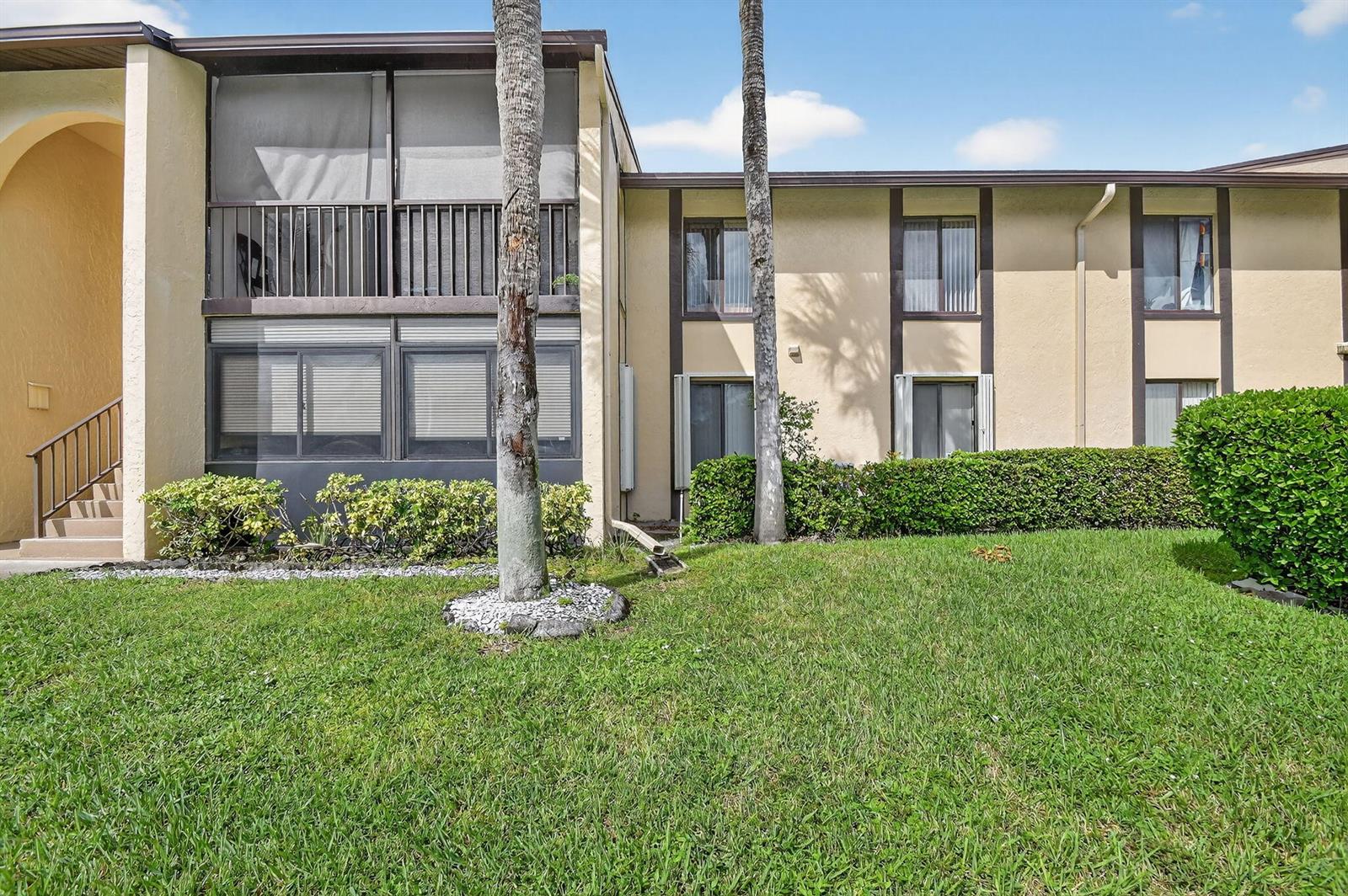 The exterior of a two-story apartment building features a screened balcony and landscaped lawn — 815 Sky Pine Way # B1, FL 33415, FL