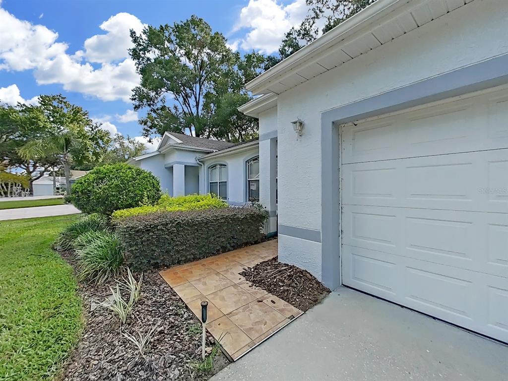 A white house exterior features a garage, a tiled walkway, and manicured landscaping — 8609 ALEXANDRA ARBOR LANE, TEMPLE TERRACE, FL