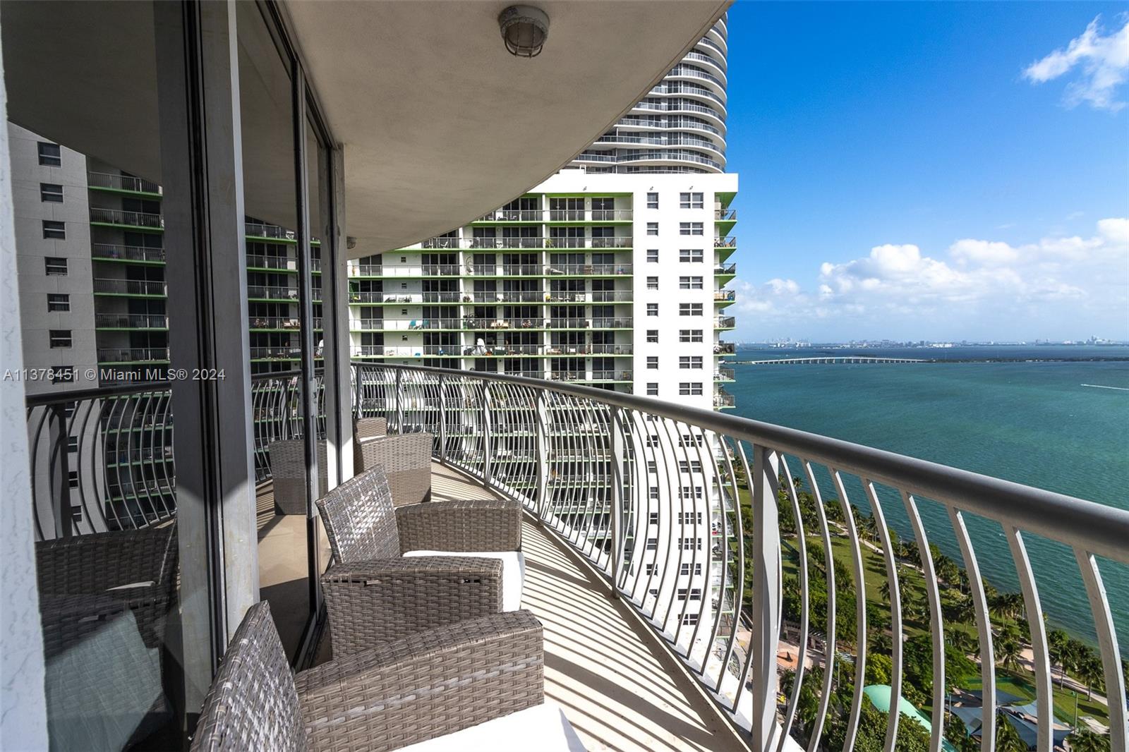 A curved balcony features wicker chairs overlooking a bay and a neighboring high-rise building — 1750 N Bayshore Dr # 3201, Miami FL 33132, MIAMI, FL