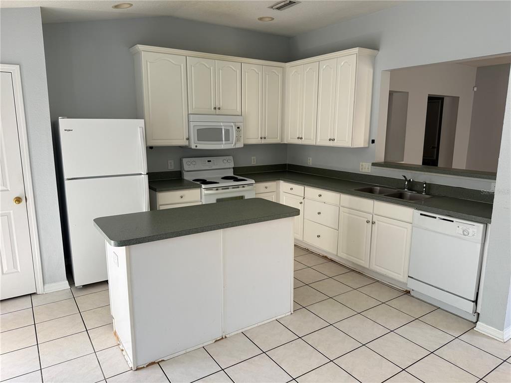 A kitchen features white cabinets, white appliances, a small island, and gray countertops — 10925 SUBTLE TRAIL DRIVE, RIVERVIEW, FL