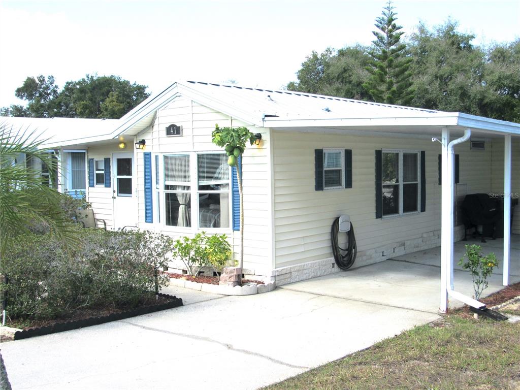 A single-story mobile home features light siding, blue shutters, a metal roof, and a carport — 50989 US HWY 27 UNIT 41, DAVENPORT, FL