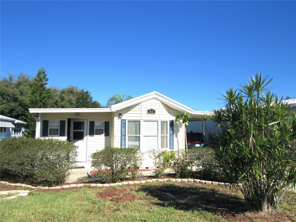 A single-story mobile home with light siding, blue shutters, and a carport under a clear sky — 50989 US HWY 27 UNIT 41, DAVENPORT, FL