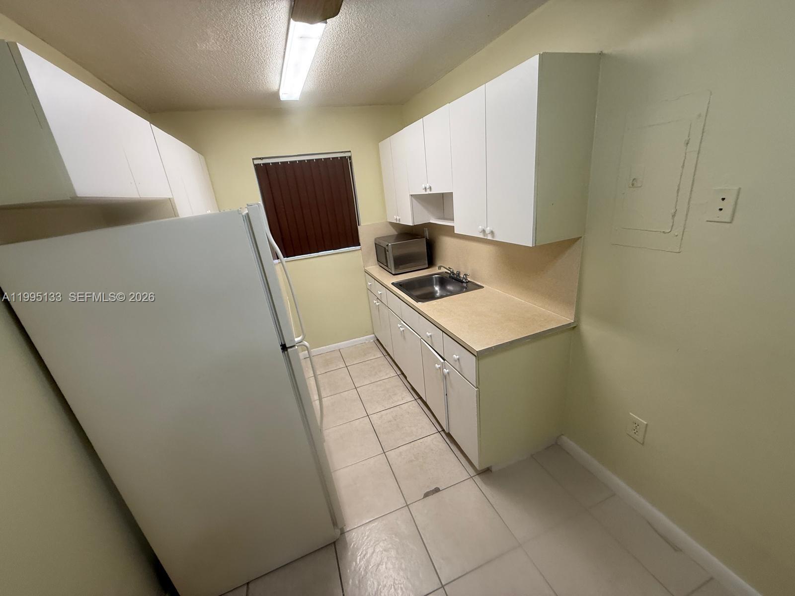 A small kitchen features white cabinets, a stainless steel sink, and light-colored tile flooring — 17530 NW 68th Ave # C4013, Hialeah FL 33015, HIALEAH, FL