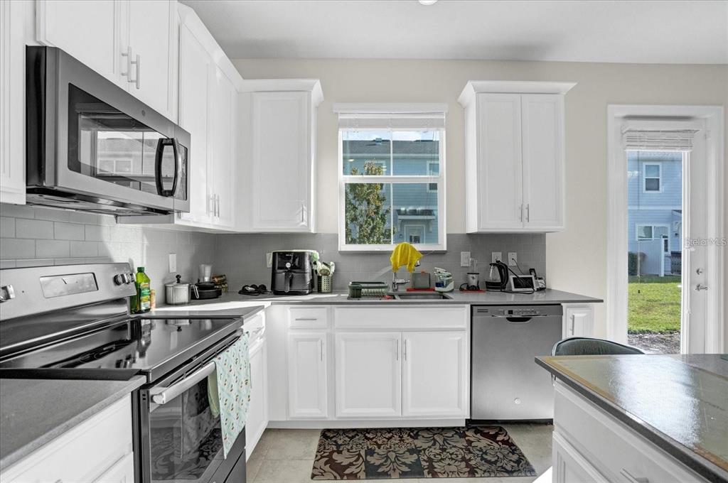 A kitchen with white cabinets, stainless steel appliances, gray countertops, and a subway tile backsplash — 2909 THEME STREET, KISSIMMEE, FL