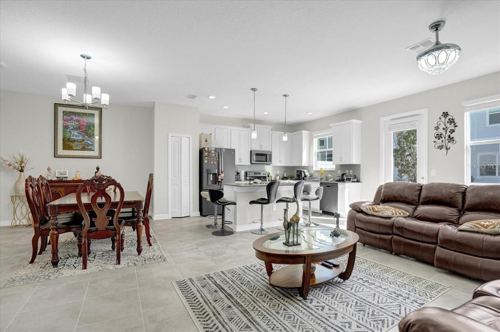 An open-concept kitchen, dining area, and living room with tile flooring and white cabinetry — 2909 THEME STREET, KISSIMMEE, FL