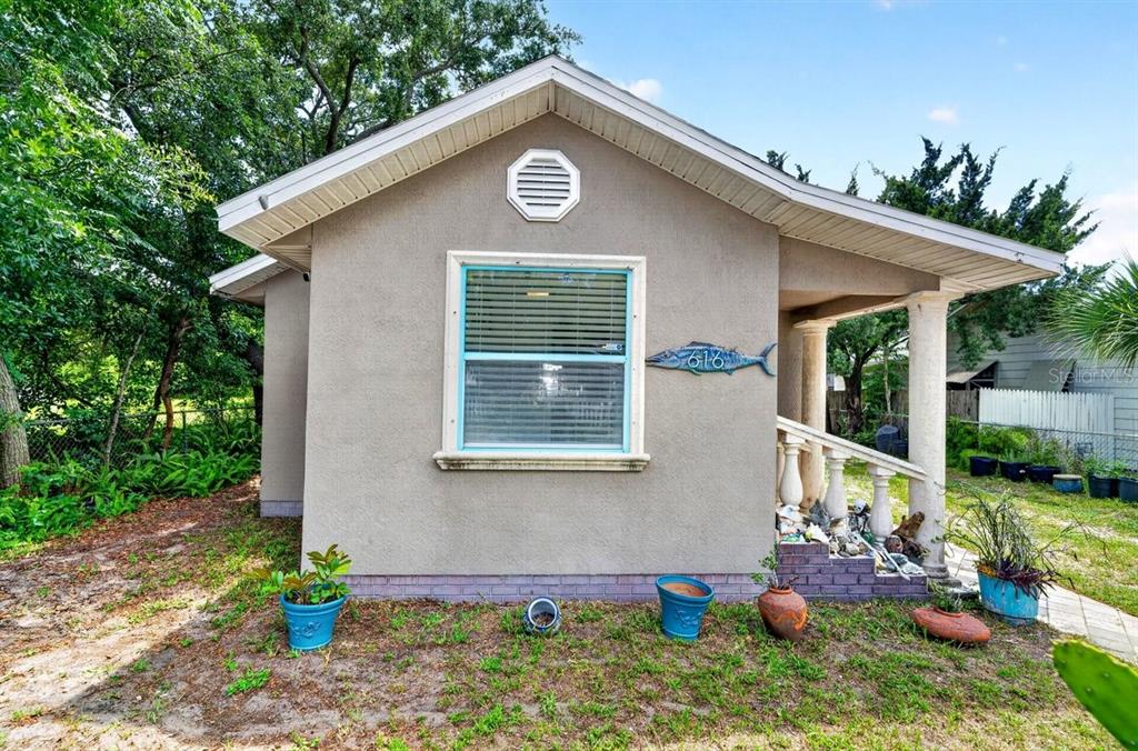 The exterior of a small, tan-colored house features a front porch with columns and a fish-shaped sign — 616 DORA STREET, NEW SMYRNA BEACH, FL