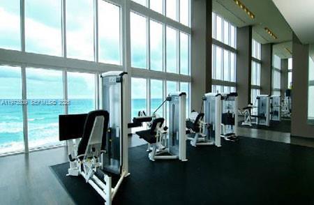 A modern fitness center features multiple exercise machines facing floor-to-ceiling windows overlooking the ocean — 1800 Ocean Dr # 1408, Hallandale Beach FL 33009, HALLANDALE BEACH, FL