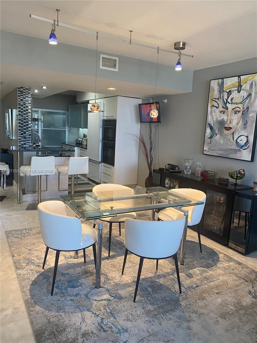 A dining area with a glass table, white chairs, and a rug near a kitchen — 1800 Ocean Dr # 1408, Hallandale Beach FL 33009, HALLANDALE BEACH, FL