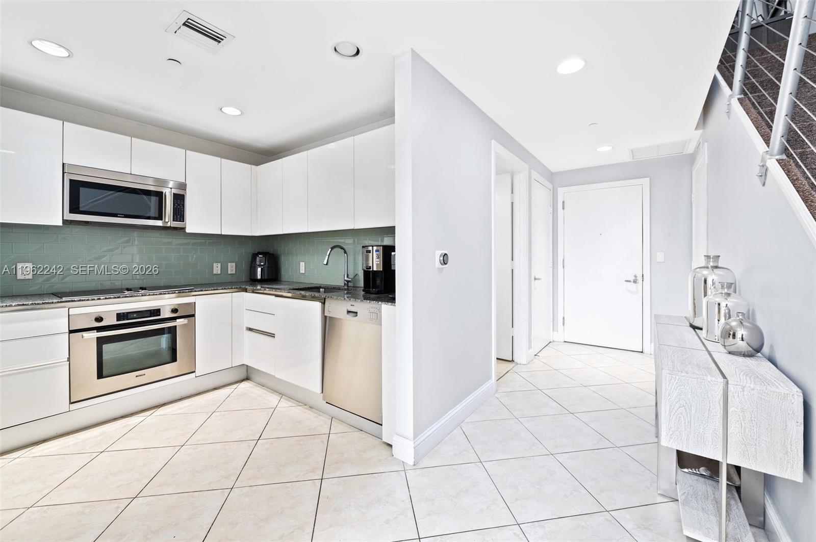 A modern kitchen features white cabinets, stainless steel appliances, and a green subway tile backsplash — 1050 Brickell Ave # 1014, Miami FL 33131, MIAMI, FL