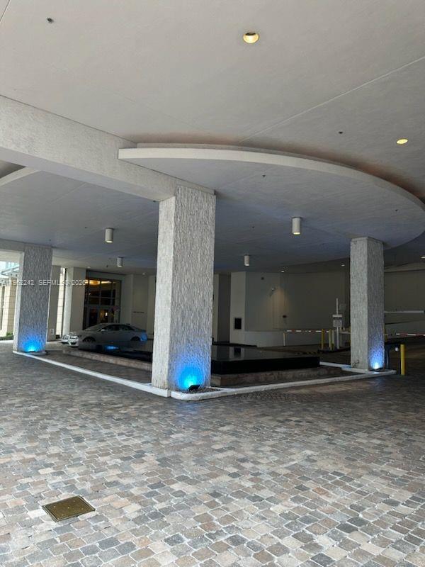 A covered building entrance features stone pillars, blue uplighting, and a cobblestone driveway — 1050 Brickell Ave # 1014, Miami FL 33131, MIAMI, FL