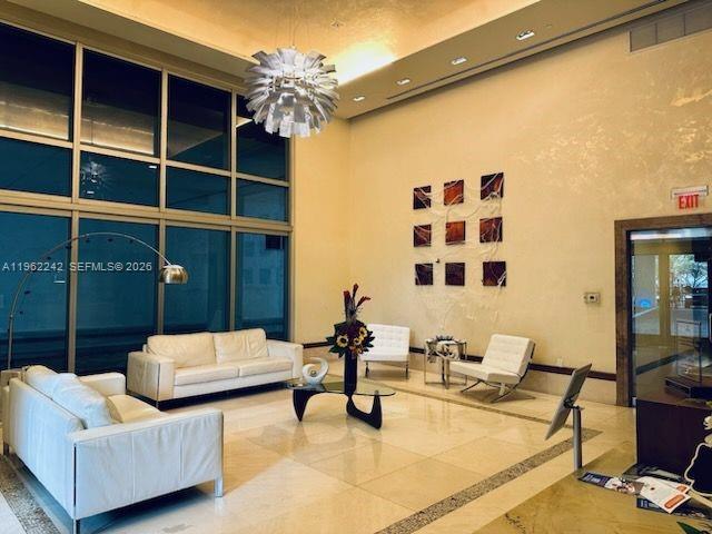 A modern lobby features white leather sofas, a glass coffee table, and a large chandelier — 1050 Brickell Ave # 1014, Miami FL 33131, MIAMI, FL