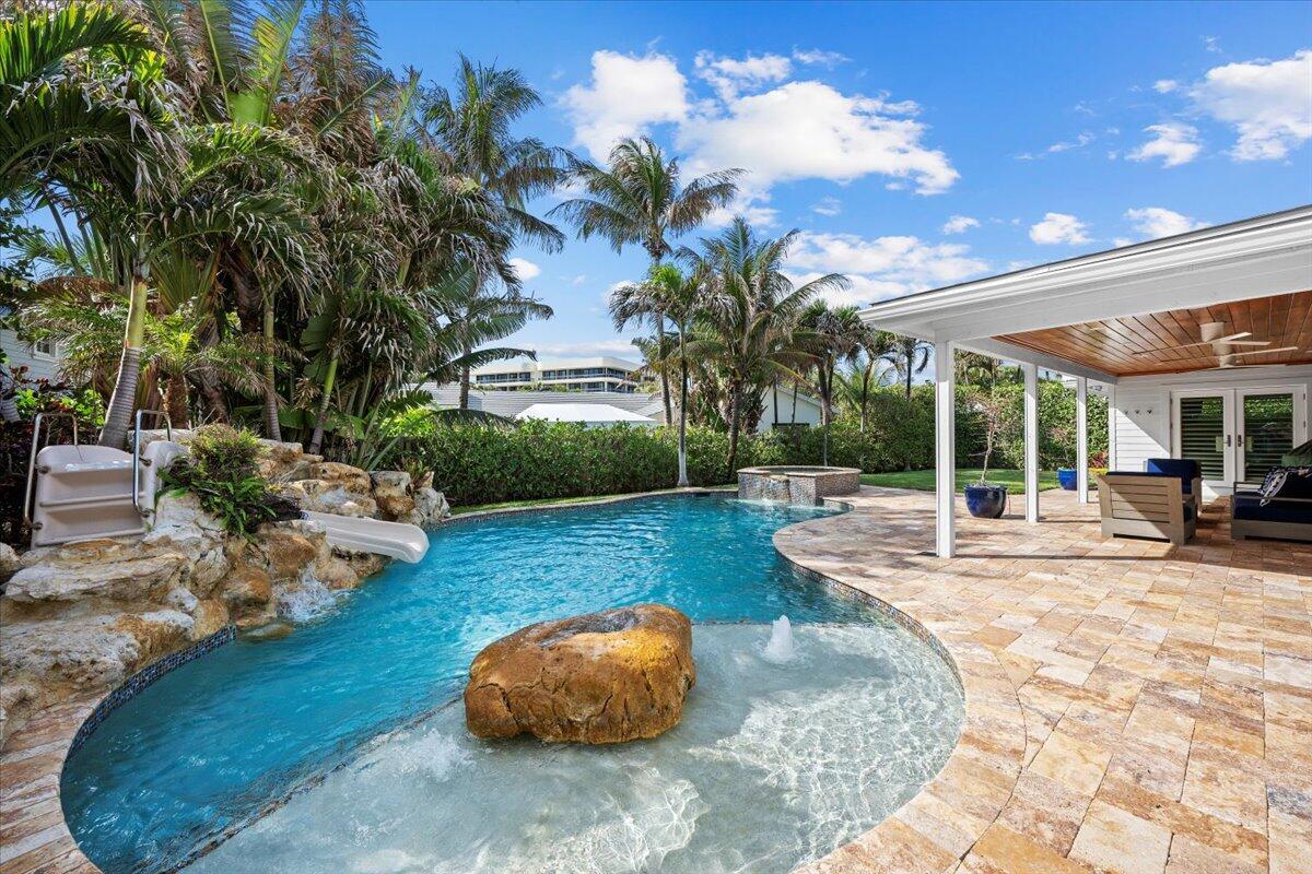 A backyard swimming pool with a rock waterfall, slide, and a covered patio area — 48 Ocean Drive, Jupiter FL 33469, JUPITER, FL