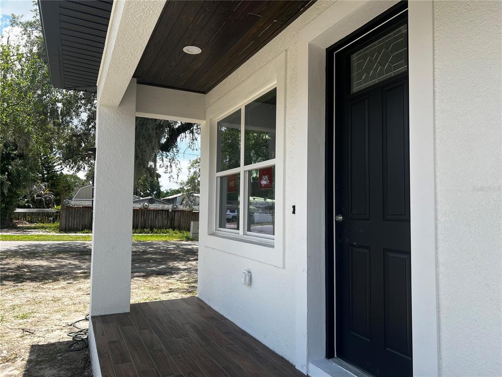 A covered front porch features wood-look tile flooring, a dark wood ceiling, and a black door — 1514 E JUNEAU STREET, TAMPA, FL