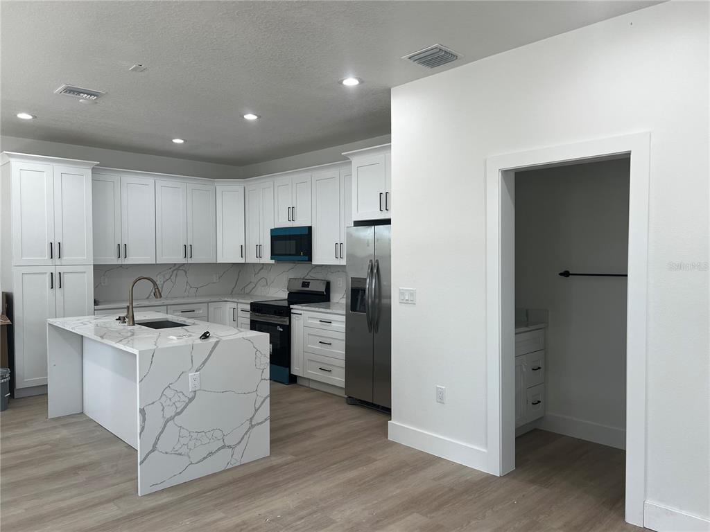 A modern kitchen features white cabinets, a marble-patterned island, and stainless steel appliances — 1514 E JUNEAU STREET, TAMPA, FL