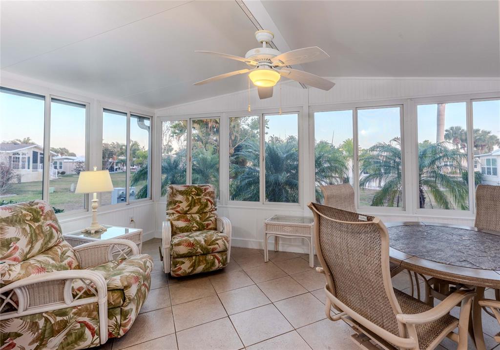 A sunroom features tile flooring, a ceiling fan, wicker furniture, and large windows overlooking palms — 2100 KINGS HIGHWAY UNIT 437, PUNTA GORDA, FL