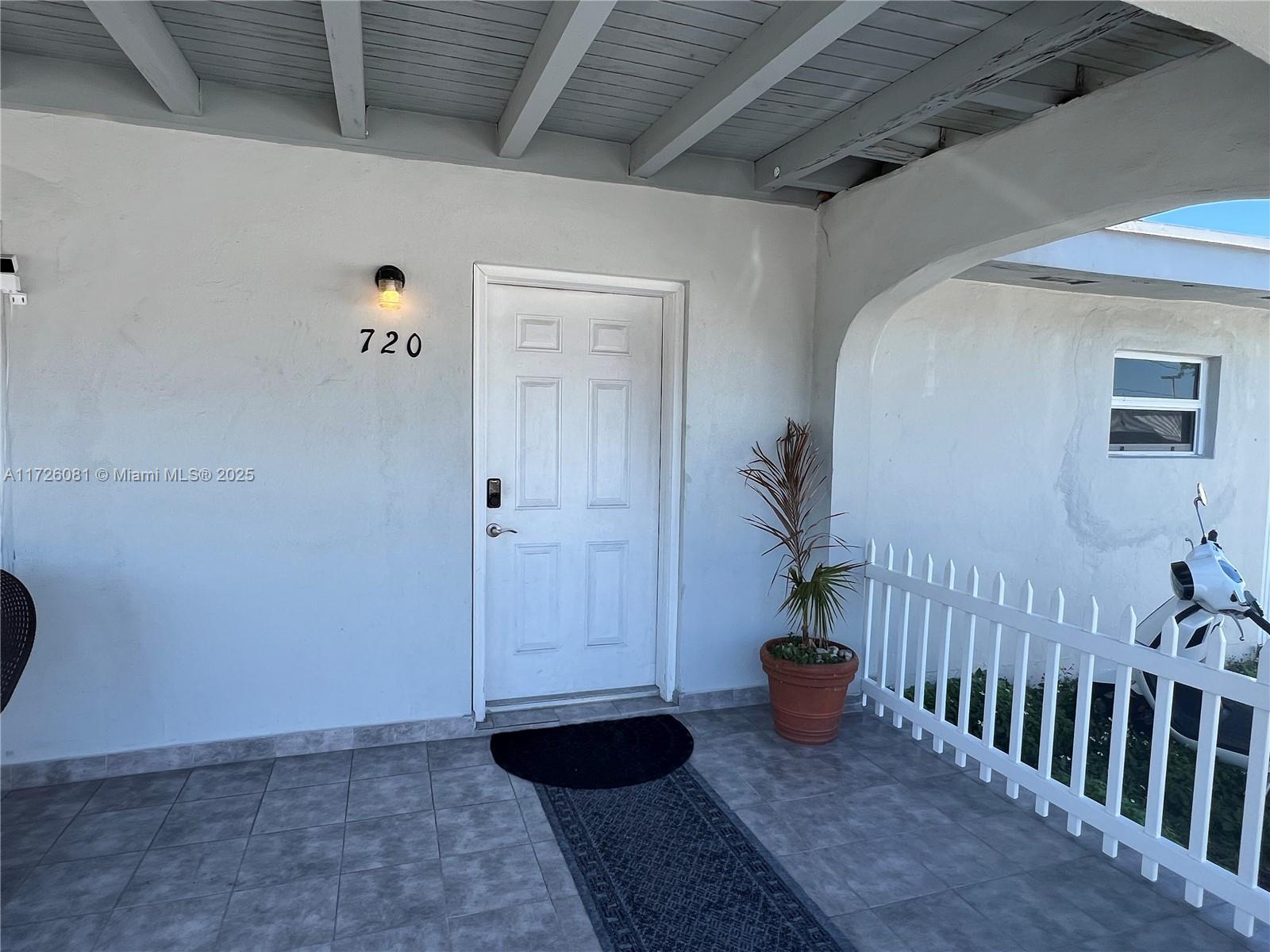 A white front door with the number 720 sits on a tiled porch with a fence — 720 NW 30th Ave, Miami FL 33125, MIAMI, FL