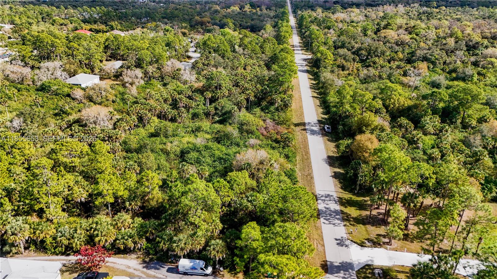 An aerial view shows a paved road running through a dense, wooded residential area — 3132 SE 24 Ave, Naples FL 34117, NAPLES, FL