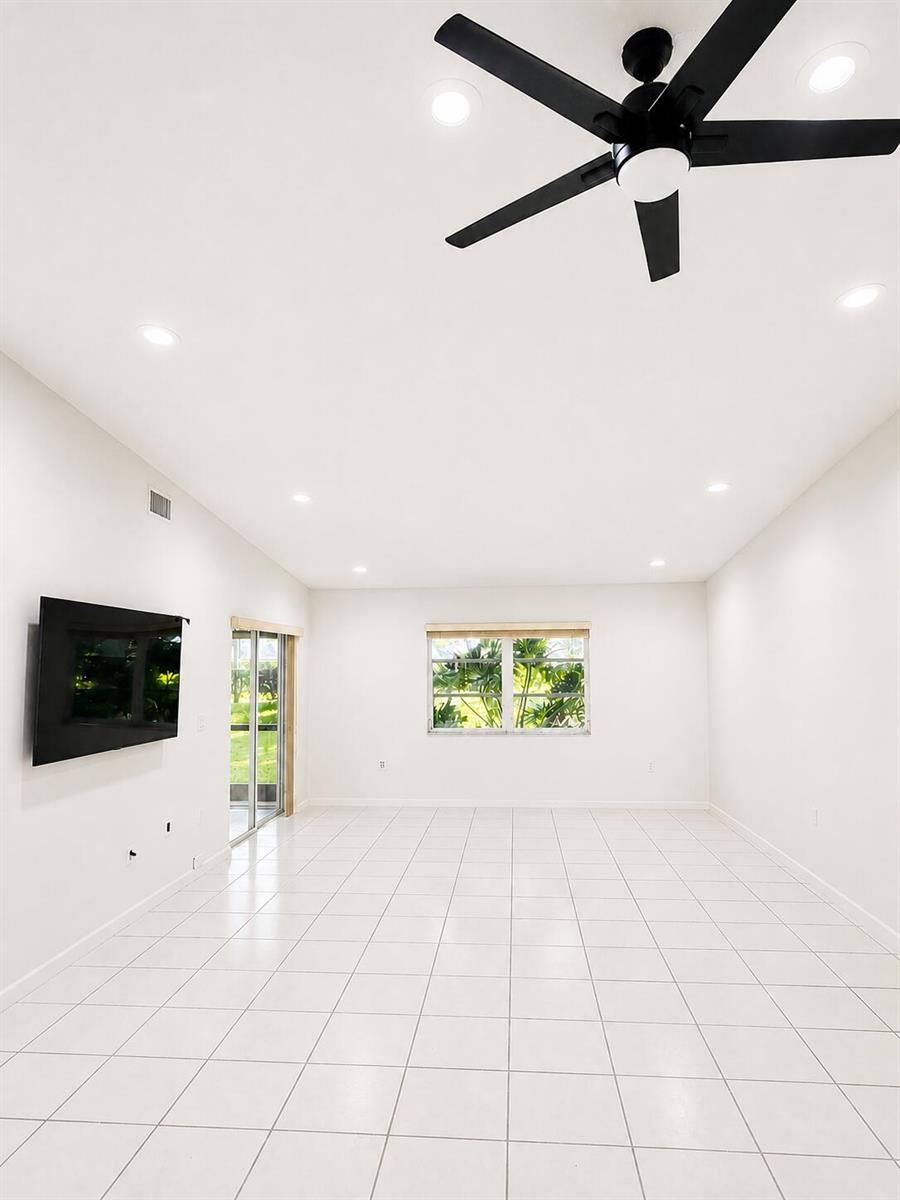A bright, empty room features white tile flooring, a ceiling fan, and a wall-mounted television — 6356 Pointe Pleasant Circle, Delray Beach FL 33484, DELRAY BEACH, FL