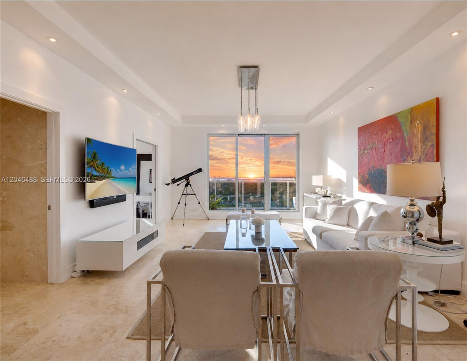 A bright living room features a white sofa, glass coffee table, and a sunset balcony view — 2301 Collins Ave, Miami Beach FL 33139, MIAMI BEACH, FL