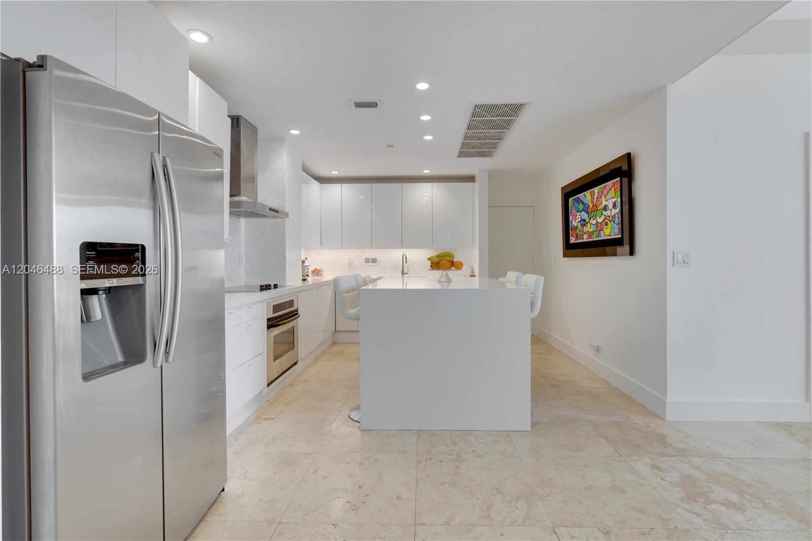 A modern kitchen features white cabinetry, a central island, stainless steel appliances, and tile flooring — 2301 Collins Ave, Miami Beach FL 33139, MIAMI BEACH, FL