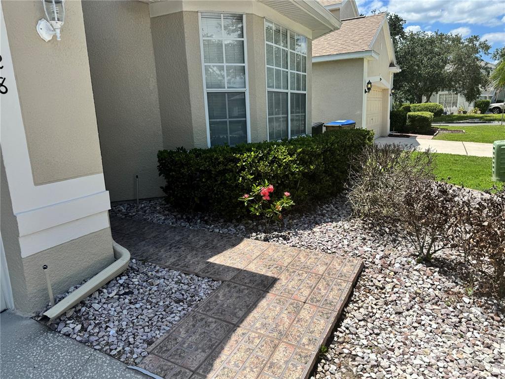 A walkway made of square pavers leads toward the front entrance of a beige house — 128 WESTMORELAND CIRCLE, KISSIMMEE, FL