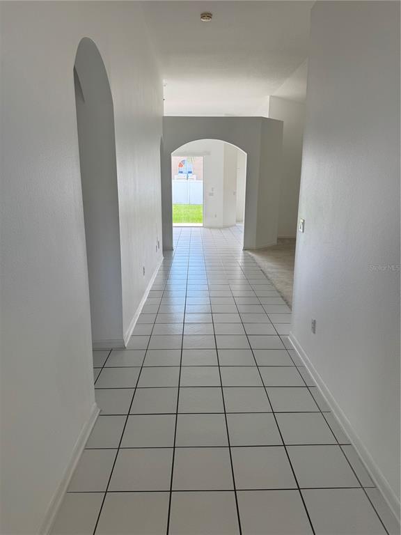 A tiled hallway leads through an arched doorway toward a view of a backyard — 128 WESTMORELAND CIRCLE, KISSIMMEE, FL