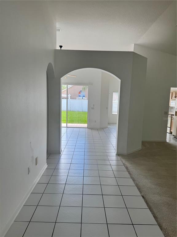 A tiled hallway leads through an arched opening toward a sliding glass door and backyard — 128 WESTMORELAND CIRCLE, KISSIMMEE, FL