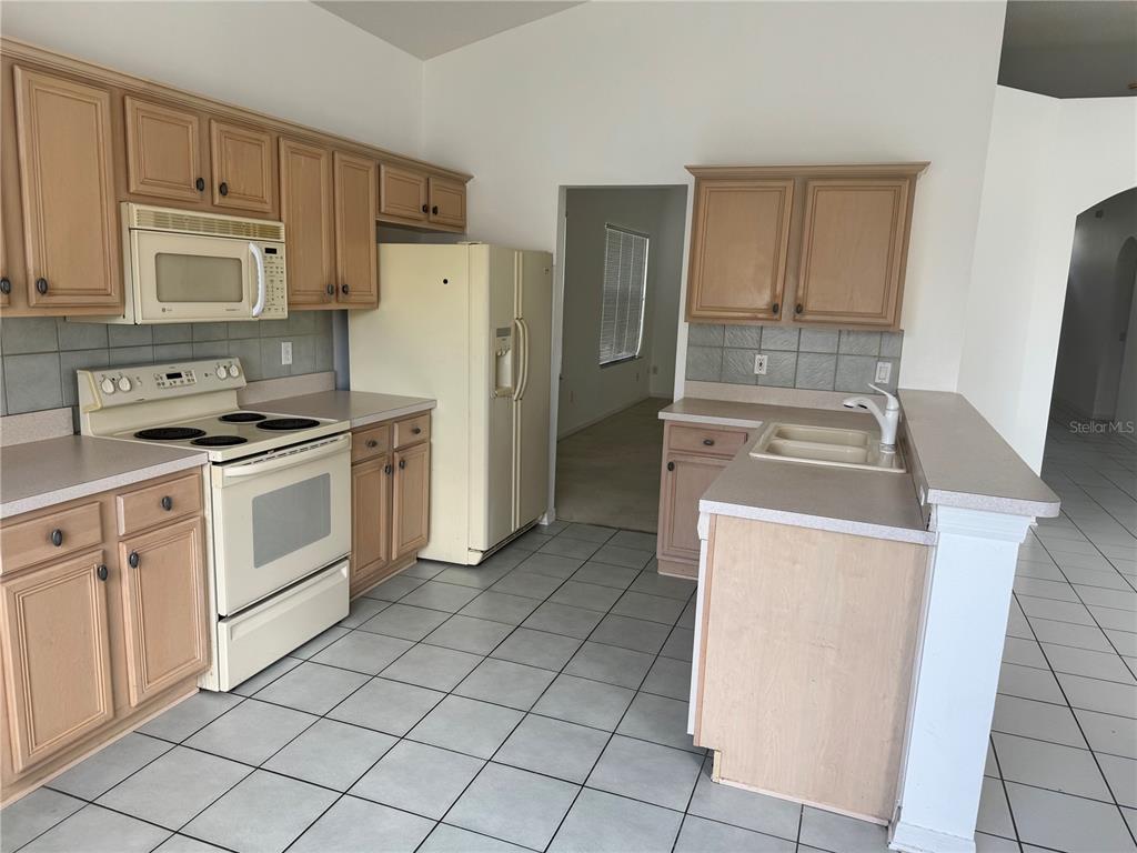A kitchen with light wood cabinets, white appliances, tile flooring, and a peninsula sink — 128 WESTMORELAND CIRCLE, KISSIMMEE, FL