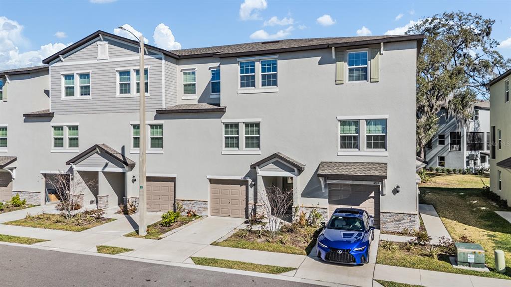 An exterior view of a multi-story townhouse complex with attached garages and a parked car — 4607 TUSCAN LOON DRIVE, TAMPA, FL