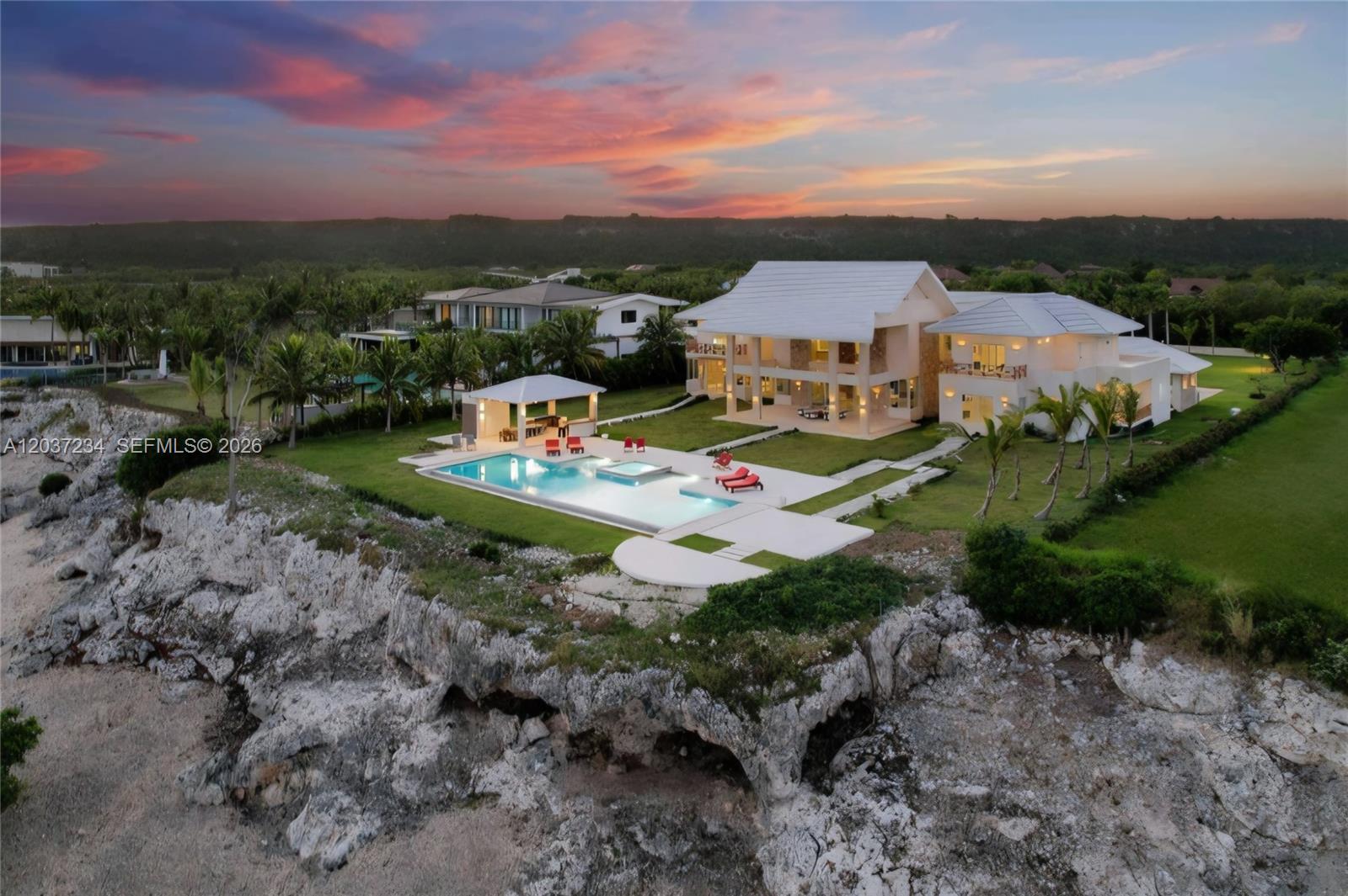 An aerial view shows a white multi-story house with a pool and patio on a cliff — 0 Lush greenery, FL, FL