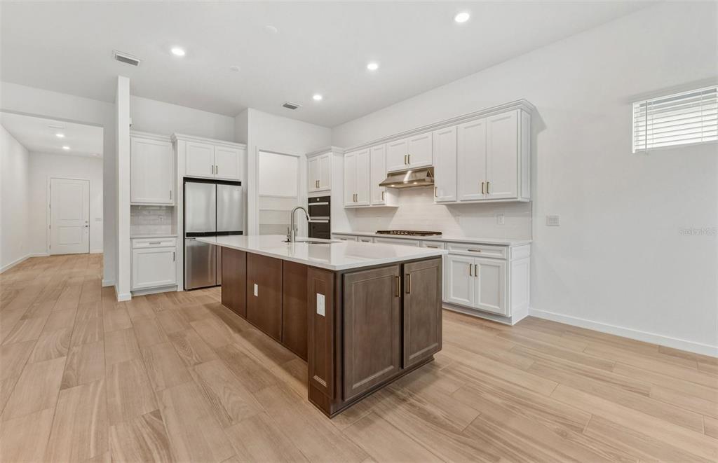 A kitchen features white cabinets, a dark wood island, stainless steel appliances, and wood-look flooring — 13622 CANYON RIDGE ROAD, SPRING HILL, FL