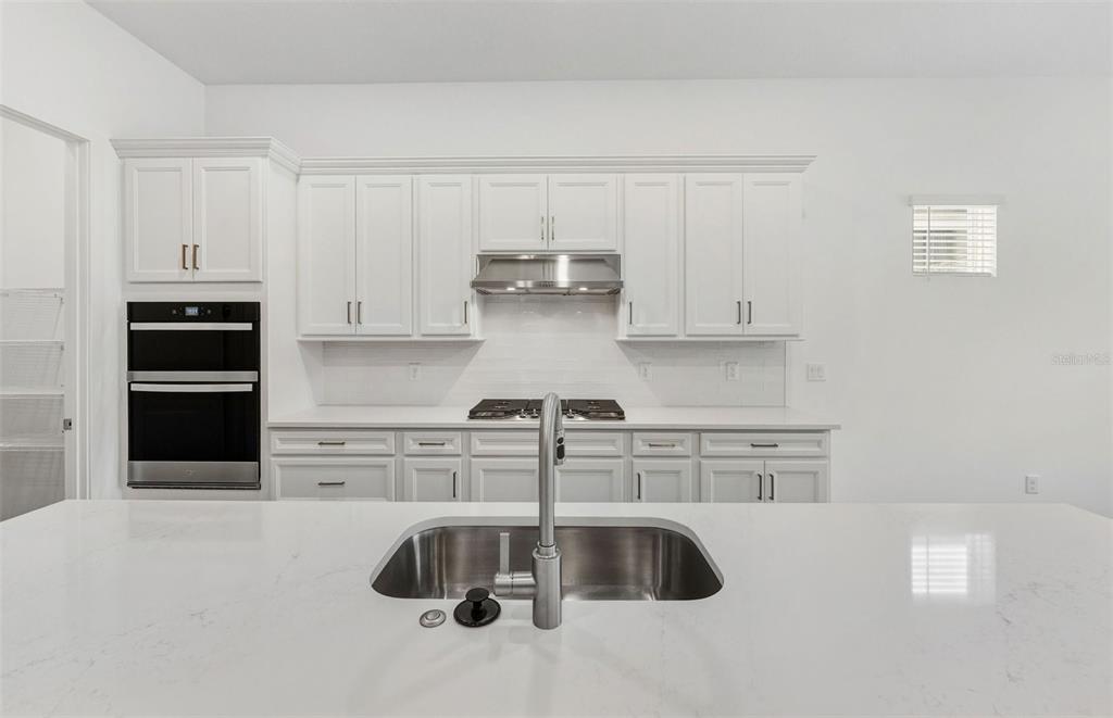 A modern kitchen features white cabinetry, stainless steel appliances, and a large quartz-topped island — 13622 CANYON RIDGE ROAD, SPRING HILL, FL
