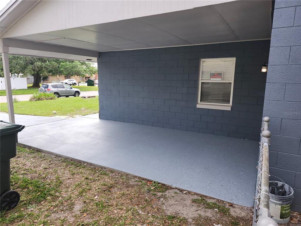 A covered carport with a gray painted concrete floor and a blue concrete block wall — 417 BENITA STREET, KISSIMMEE, FL