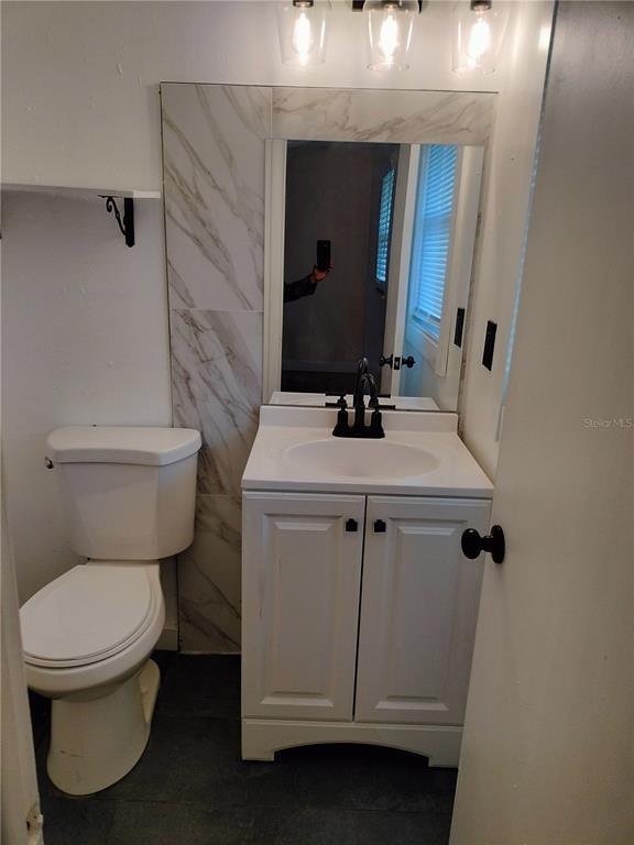 A bathroom features a white vanity, marble-look tile backsplash, mirror, and a toilet — 417 BENITA STREET, KISSIMMEE, FL