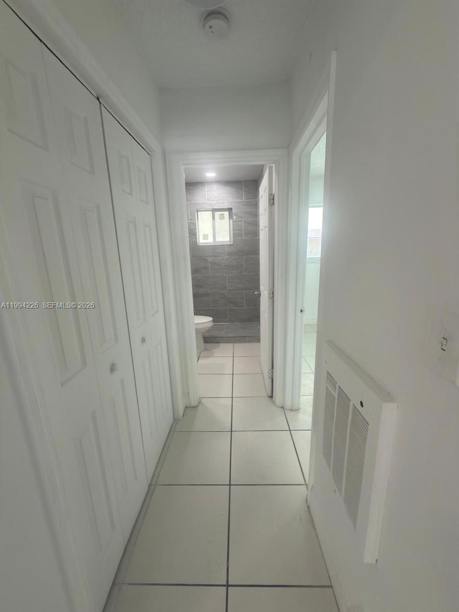 A narrow hallway with white tile floors leads to a bathroom with gray tiled walls — 2622 NW 24th St # 3B, Miami FL 33142, MIAMI, FL