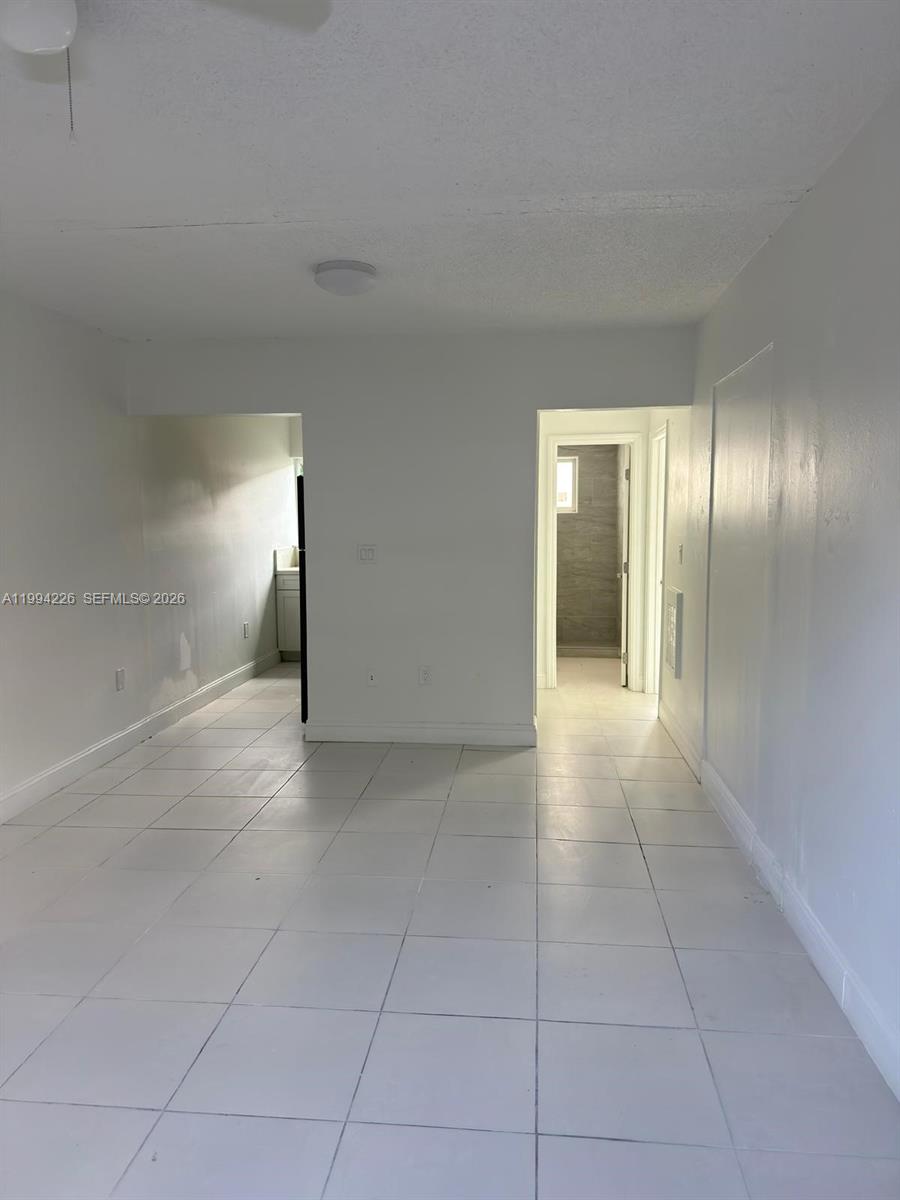 A room with white walls and light-colored tile flooring leads to a kitchen and bathroom — 2622 NW 24th St # 3B, Miami FL 33142, MIAMI, FL