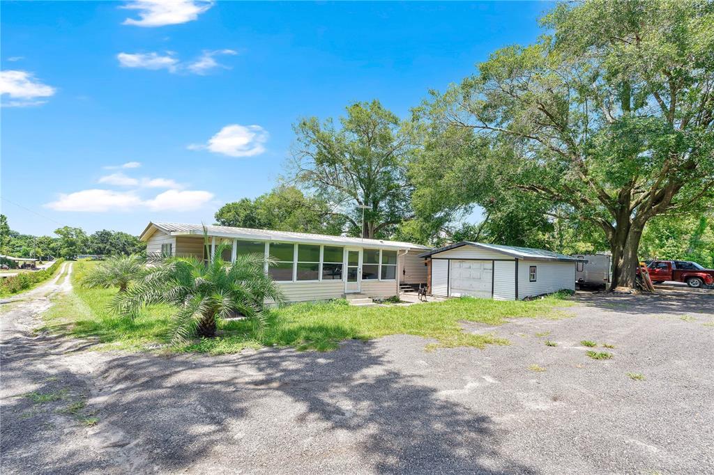 A single-story house with a screened porch and adjacent garage sits on a gravel lot — 4850 W PONKAN ROAD, APOPKA, FL