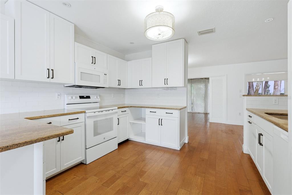A white kitchen features granite countertops, wood flooring, and a central pendant light fixture — 5273 VILLA MAJORCA COURT UNIT 25, SARASOTA, FL