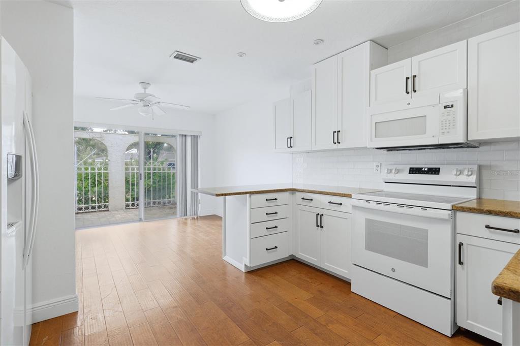 A kitchen with white cabinets, granite countertops, and wood flooring opens to a patio area — 5273 VILLA MAJORCA COURT UNIT 25, SARASOTA, FL