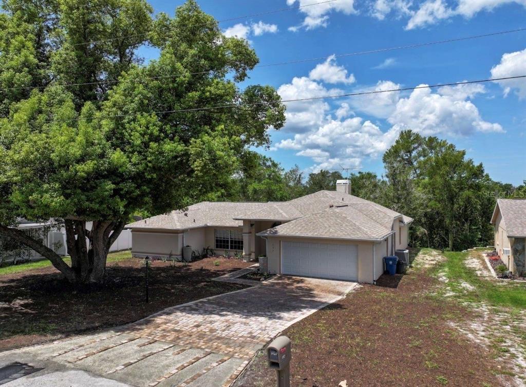 A single-story house with a paved driveway, a large tree, and a two-car garage — 5137 MONTFORD CIRCLE, SPRING HILL, FL