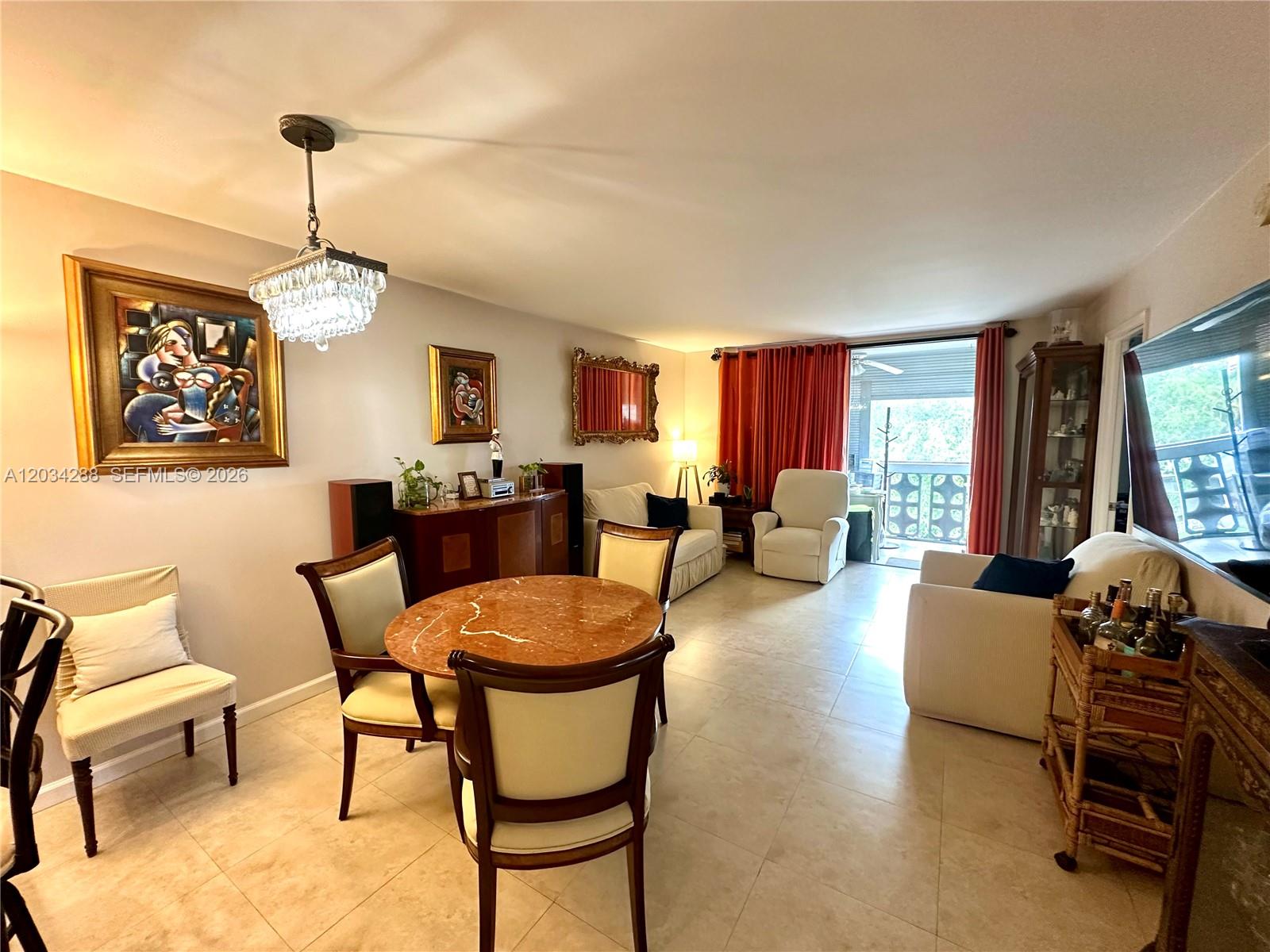 A living and dining area features tile floors, a crystal chandelier, and a balcony view — 211 NE 8th Ave # 304, Hallandale Beach FL 33009, HALLANDALE BEACH, FL