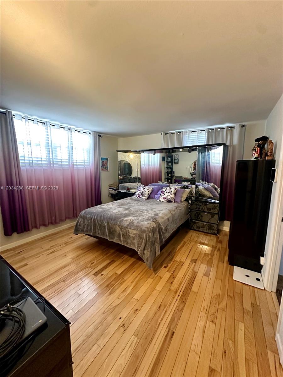 A bedroom features hardwood floors, a bed with a mirrored headboard, and purple ombre curtains — 211 NE 8th Ave # 304, Hallandale Beach FL 33009, HALLANDALE BEACH, FL