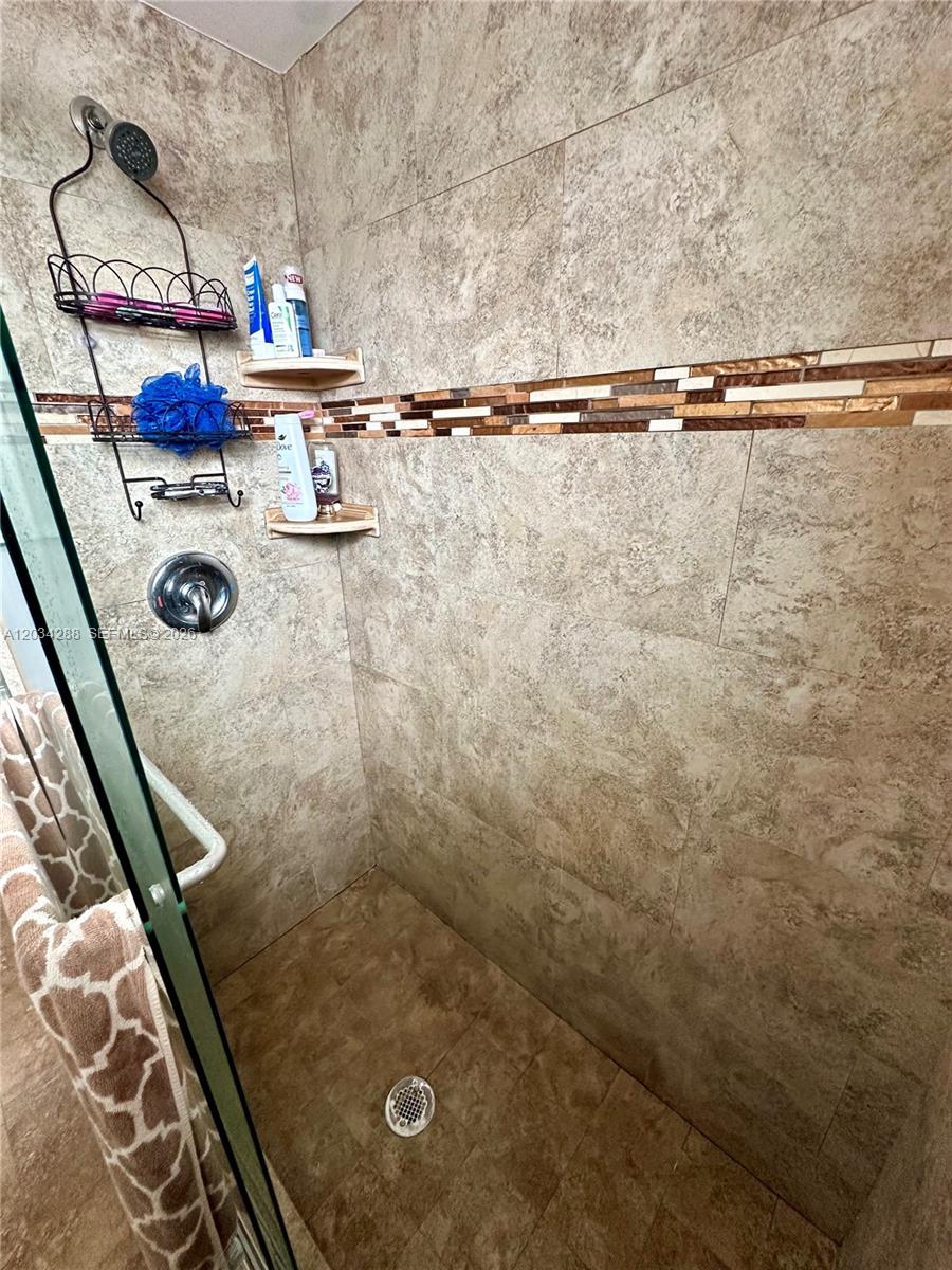 A walk-in shower features tan stone-look tile walls, a decorative mosaic accent strip, and shelving — 211 NE 8th Ave # 304, Hallandale Beach FL 33009, HALLANDALE BEACH, FL