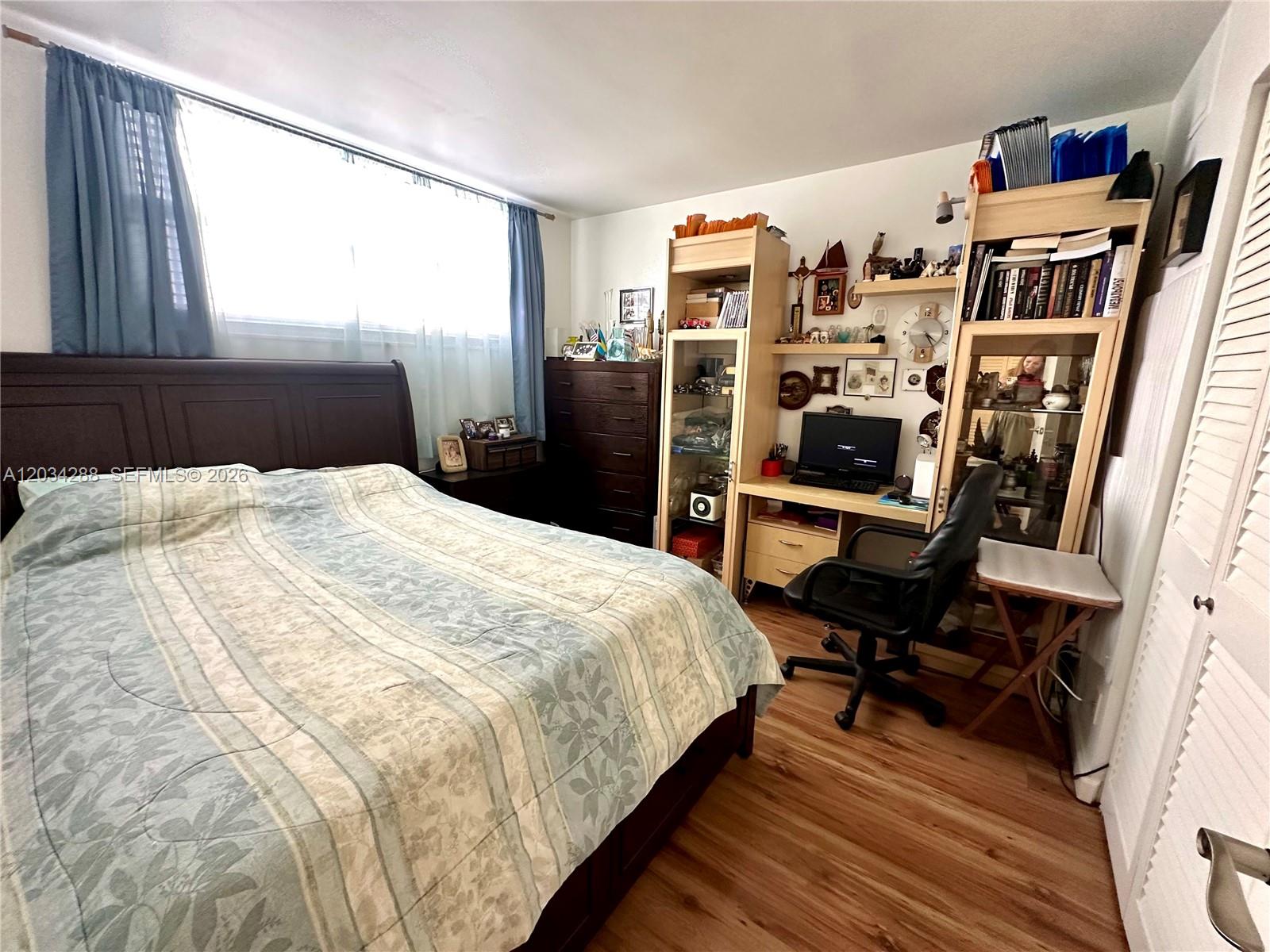 A bedroom features a bed, a desk with a computer, shelving units, and wood-look flooring — 211 NE 8th Ave # 304, Hallandale Beach FL 33009, HALLANDALE BEACH, FL